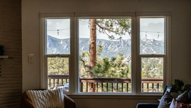 Ein Zimmer mit großem Fenster und Blick auf eine gebirgige Landschaft, einer Holzdielen-Terrasse und zwei Ledersesseln.