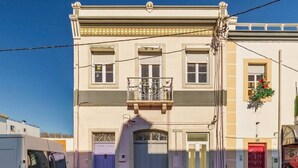 A two-story building with a balcony, a red door, and a white van parked in front. - Garrett Premium Setúbal (Setúbal)