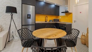 A modern kitchen with dark cabinets, a stainless steel refrigerator, a microwave, and a wooden dining table with four chairs. - Garrett Premium Setúbal (Setúbal)