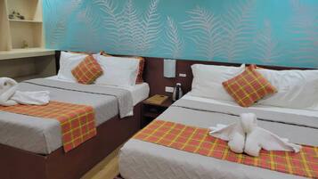 Habitación de hotel con dos camas, cada una con manta y almohadas a cuadros, una mesita con una botella, y una pared con diseño de hojas.