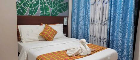 A hotel room with a bed, a headboard, a wall art of leaves, and blue patterned curtains.