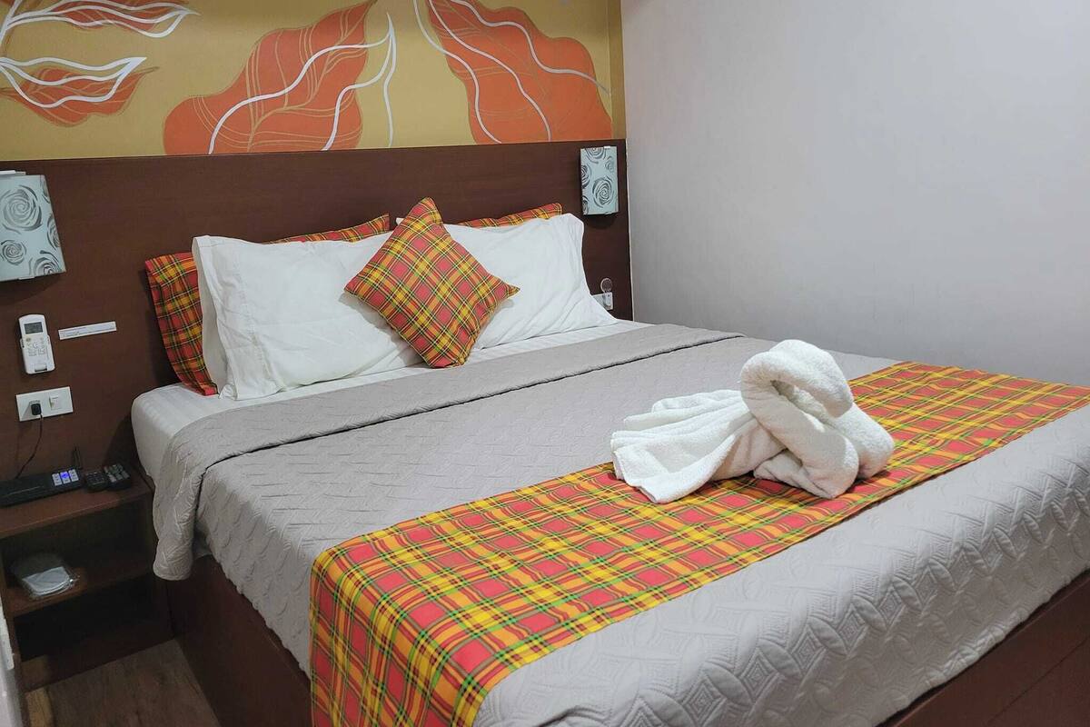 A neatly made bed with a plaid bedspread, white pillows, and a white towel on the side.