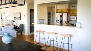 Una cocina moderna con un refrigerador de acero inoxidable, armarios de madera y una encimera. Hay tres taburetes de madera y una barra.