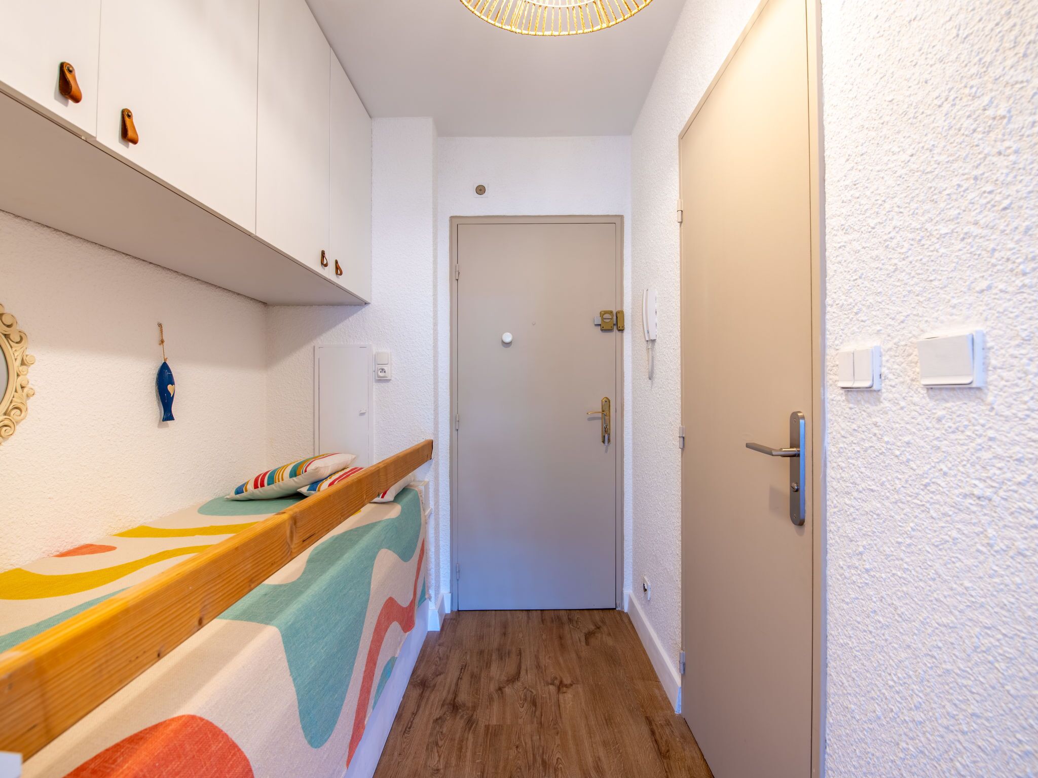 A narrow hallway with a wooden floor, a white door at the end, and a shelf with decorative items.