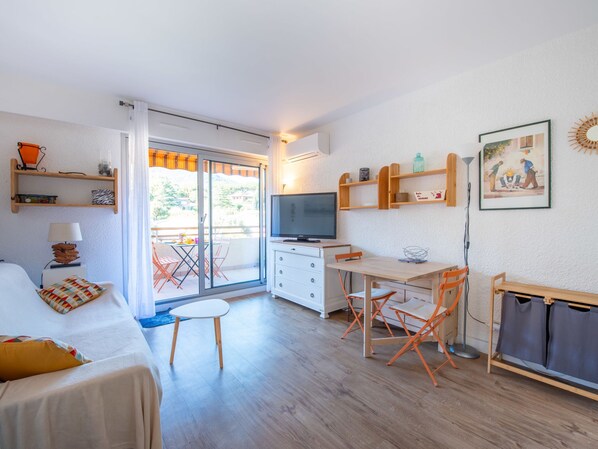 A compact hotel room with a balcony, a TV, a small dining table, and a bed.