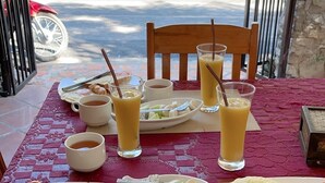 Una mesa de desayuno dispuesta con platos de huevos, tostadas y fruta, acompañada de tazas de té y jugo.