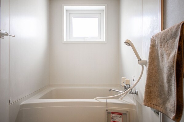 Une salle de bain avec une baignoire, une fenêtre au-dessus et une serviette accrochée au mur.