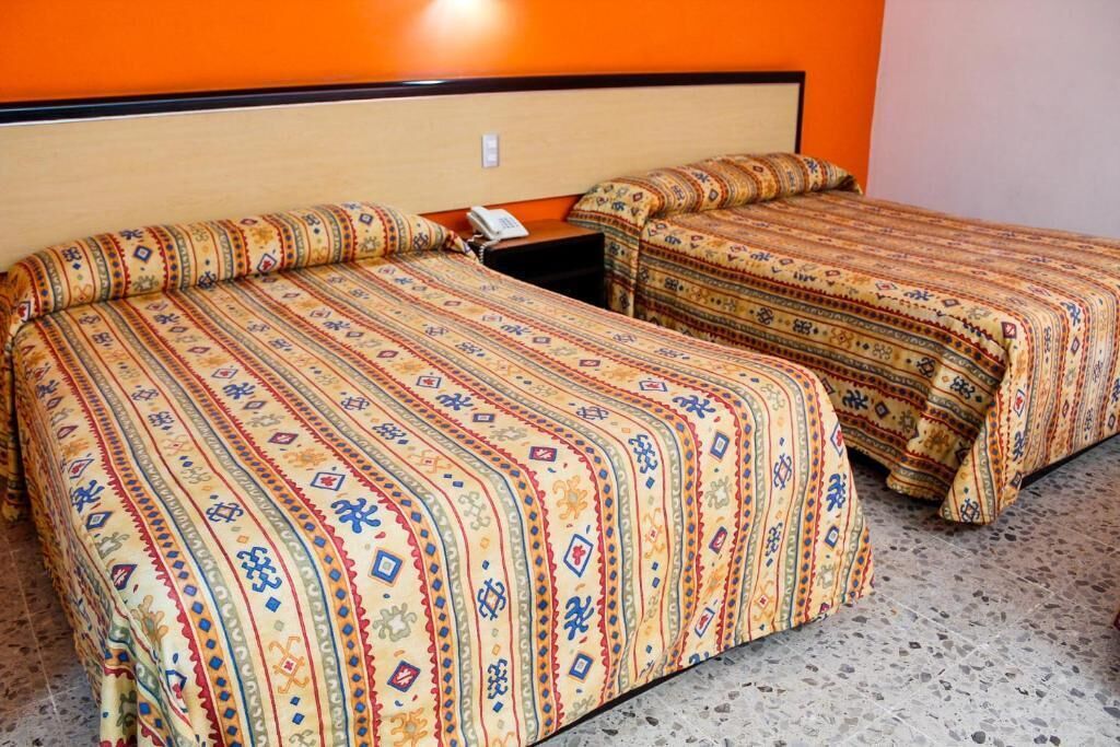 Two beds with patterned bedding in a room with orange walls and a speckled floor.
