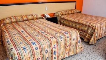 Dos camas con ropa de cama estampada en una habitación con paredes anaranjadas y suelo moteado.