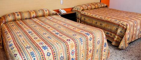 Two beds with patterned bedding in a room with orange walls and a speckled floor.