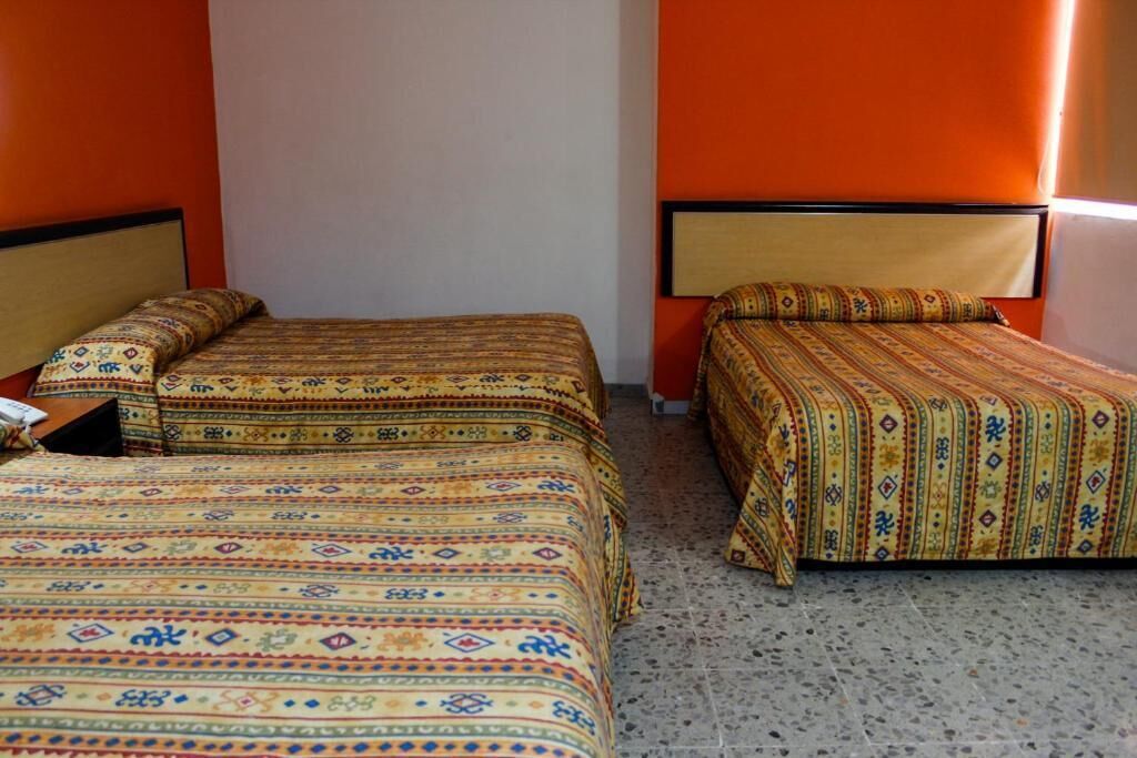 A room with two beds, each with patterned bedding, a tiled floor, and orange walls.