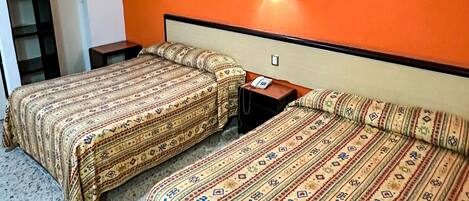 A hotel room with two beds, an orange wall, a nightstand, and a lamp.