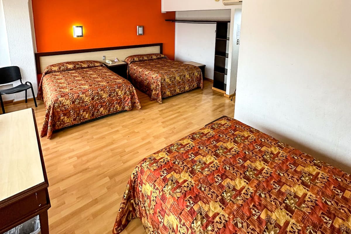 A room with two beds, a desk, a chair, and a trash bin.