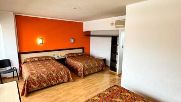 A room with two beds, a desk, a chair, and a trash bin.