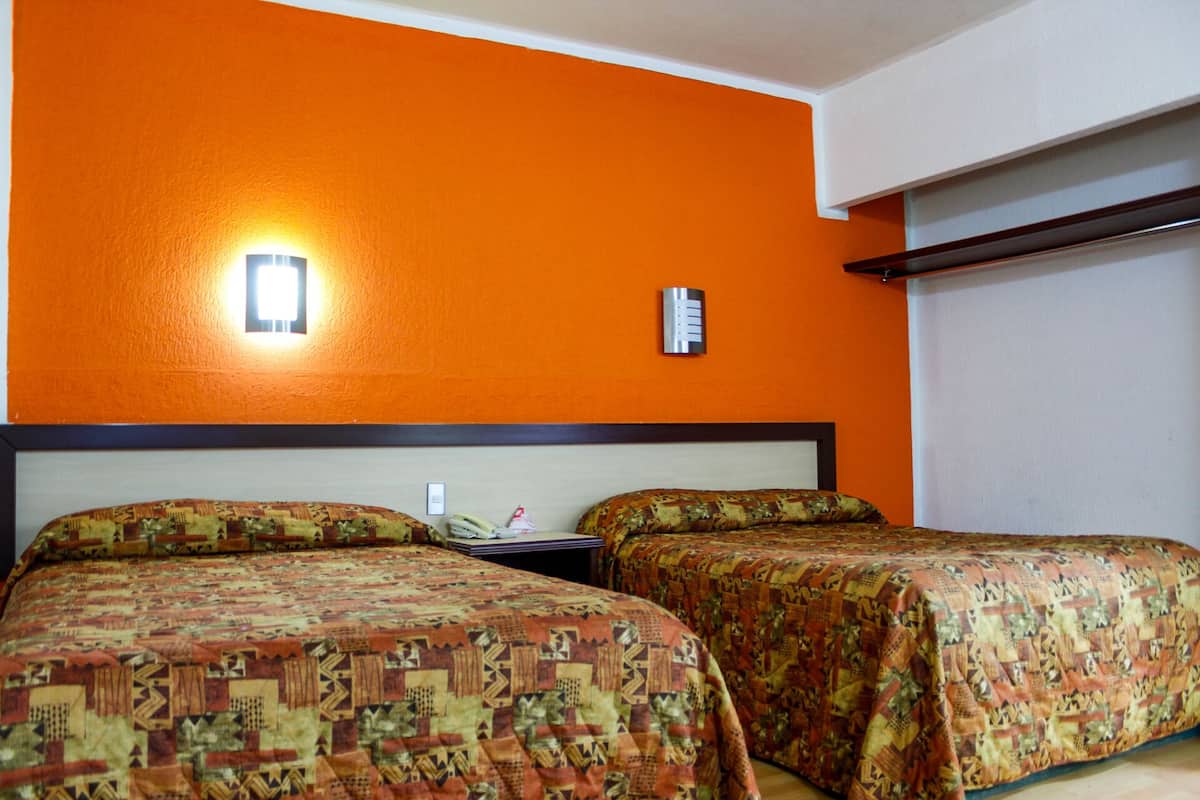 A hotel room with two beds, an orange wall, a nightstand with a phone, and a wall-mounted thermostat.