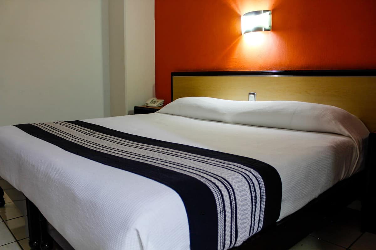 A hotel room with a bed, a nightstand, a phone, and a wall-mounted light.