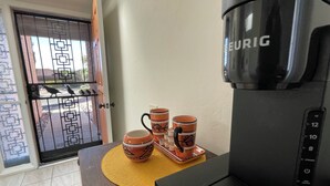 Una cafetera con cuatro tazas sobre una mesa, una puerta con reja metálica y un suelo de baldosas.