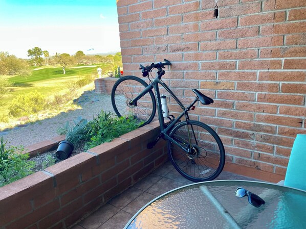 A brick wall with a bicycle leaning against it, a small garden area with plants, and a view of a golf course in the background.