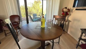 Una mesa de comedor redonda de madera, con una botella de licor y un vaso encima, rodeada de sillas.