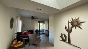 Amplia sala de estar con ventilador de techo, una mesa de comedor con sillas y una decoración de cactus colgado en la pared.