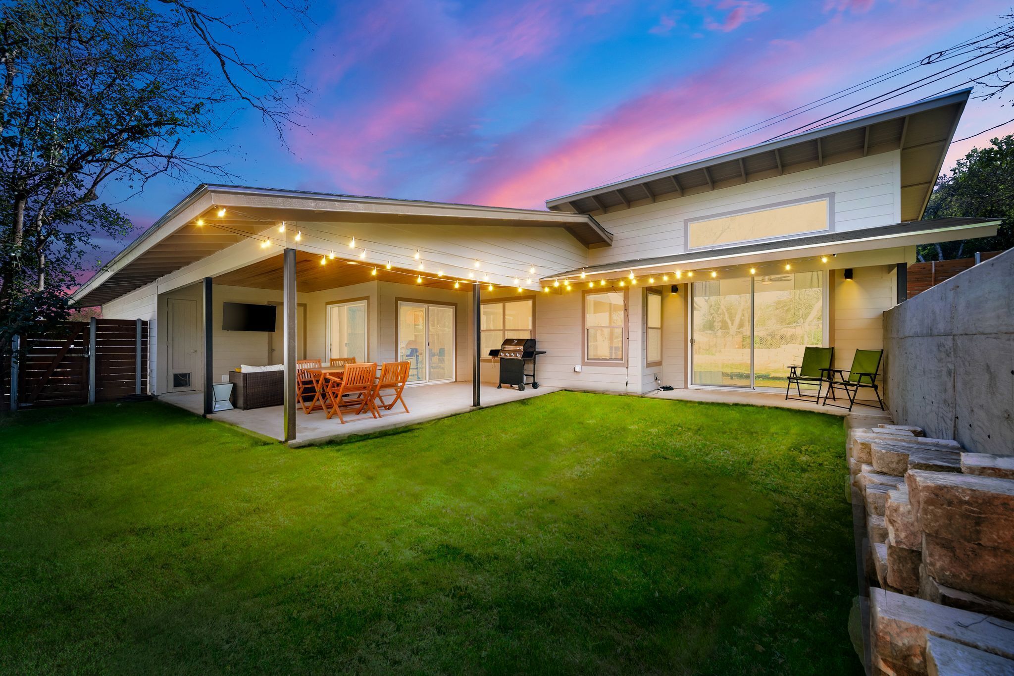 Une maison moderne dotée d’un patio couvert, d’un espace salon extérieur et d’une pelouse bien entretenue.