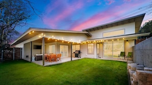 Une maison moderne dotée d’un patio couvert, d’un espace salon extérieur et d’une pelouse bien entretenue.