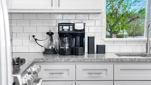 Une cuisine moderne avec des meubles blancs, un plan de travail en granit, une machine à café et une fenêtre donnant sur la forêt.
