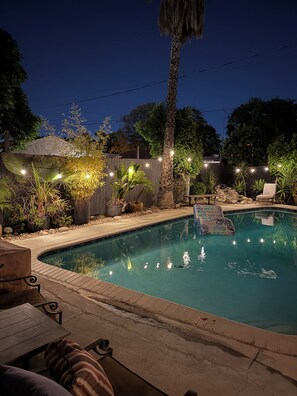 Une piscine bordée de pierres, entourée de plantes en pot et de mobilier d’extérieur.