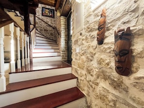 A staircase with wooden steps leading to a landing, a stone wall with two wooden carvings, and a framed picture on the wall.