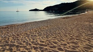 En strand med sandmönster, en båt på vattnet och ett kuperat landskap i bakgrunden.