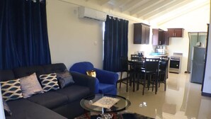 A living room with a sofa, armchair, and coffee table, a dining area with chairs and a table, and a kitchen with cabinets and appliances. - Harbour Oasis Retreat - Charming 2 Bedroom House (Old Harbour)