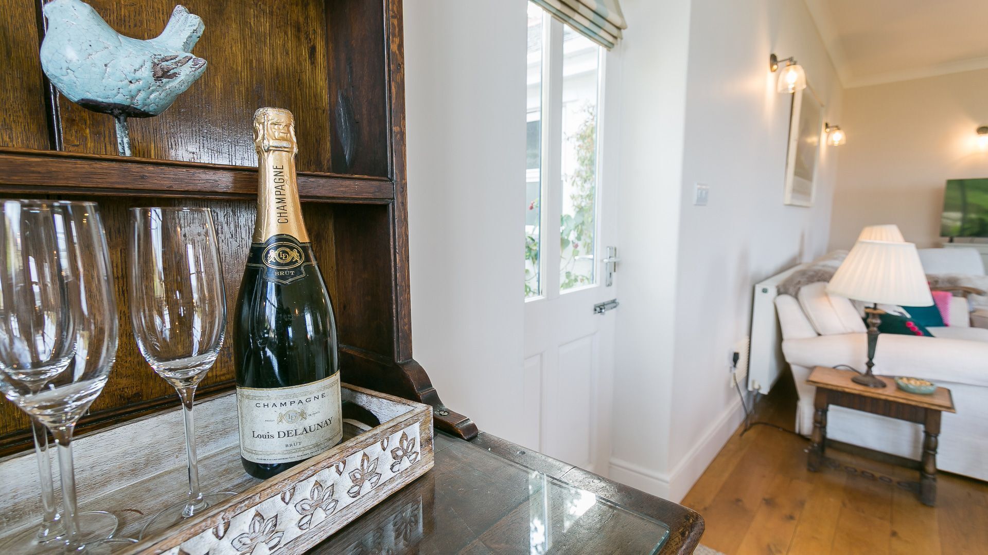 A room with a wooden table displaying a bottle of champagne and two glasses. A decorative chicken is mounted on the wall above the table.