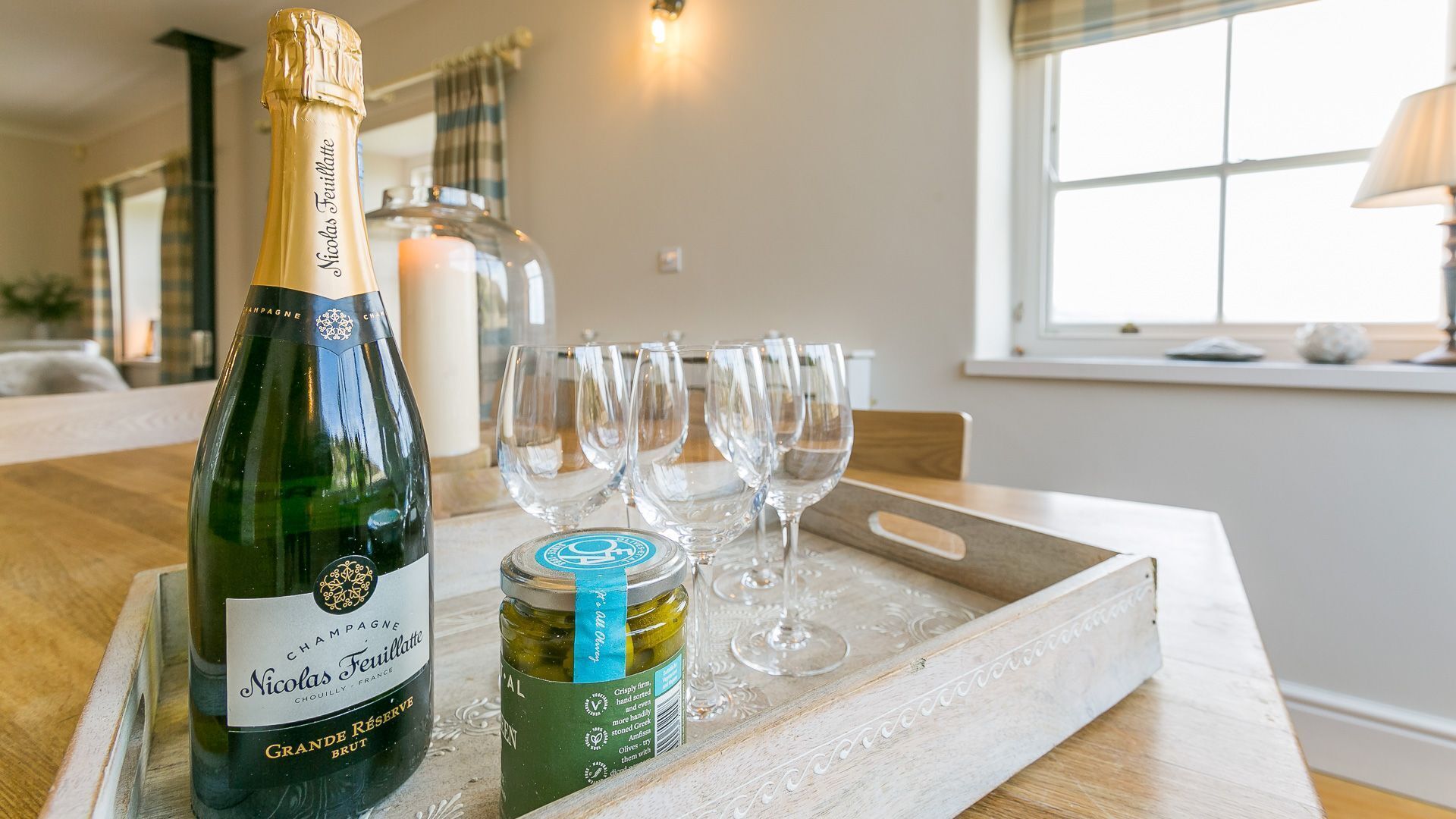 A bottle of Nicolas Feuillatte champagne, a jar of olives, and several empty wine glasses on a wooden tray.