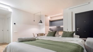 Camera da letto moderna con un letto grande, una scrivania e un angolo cottura sullo sfondo.