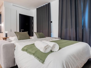 Ein Hotelzimmer mit einem Bett, einem Nachttisch, einer Lampe, einer Tür und Vorhängen.