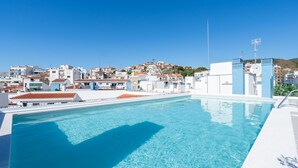 Una piscina blu cristallina con vista su una cittadina costiera e edifici sullo sfondo.