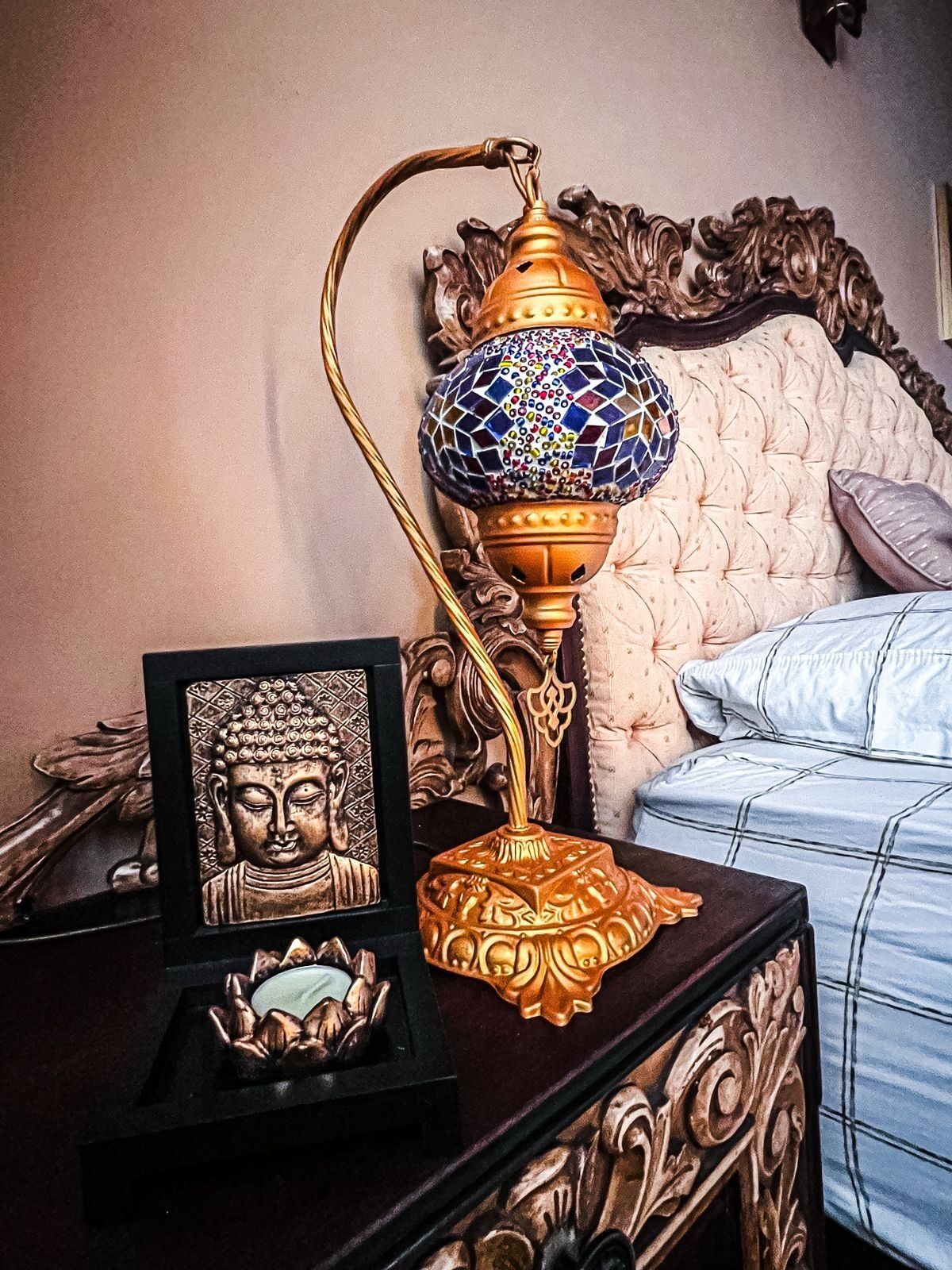 Ein Bett mit Kopfteil, ein Nachttisch mit Lampe und eine Buddha-Statue im Bilderrahmen.