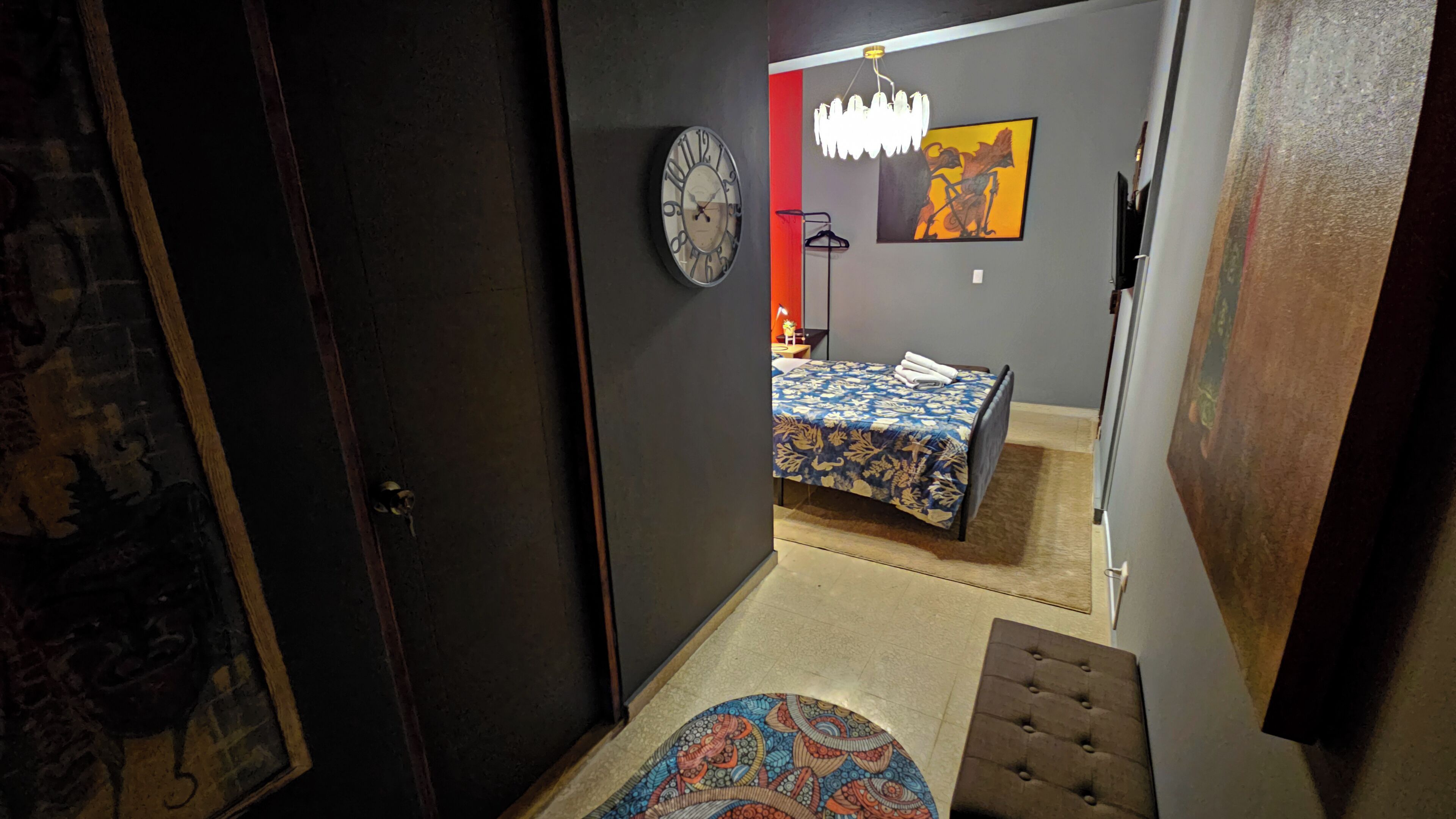 A bedroom with a bed, a clock, a painting, and a chandelier.