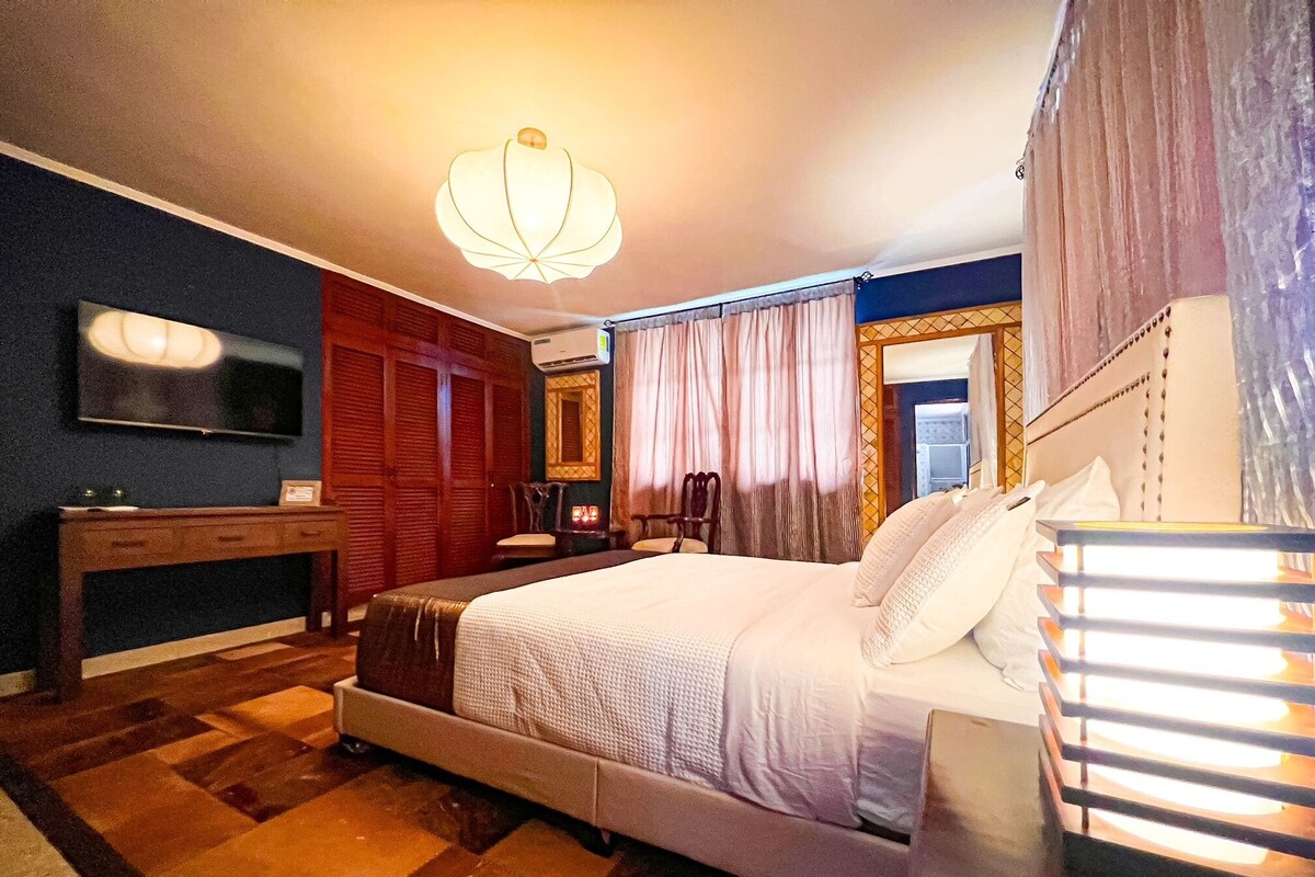 A hotel room with a large bed, a desk, a television, and a mirror.