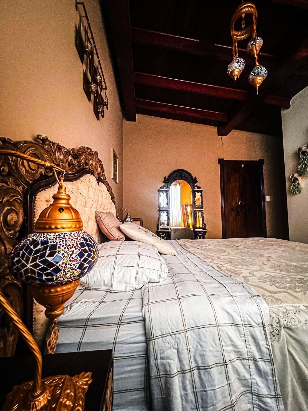 A bedroom with a large bed, ornate headboard, a decorative lamp, and a mirror.
