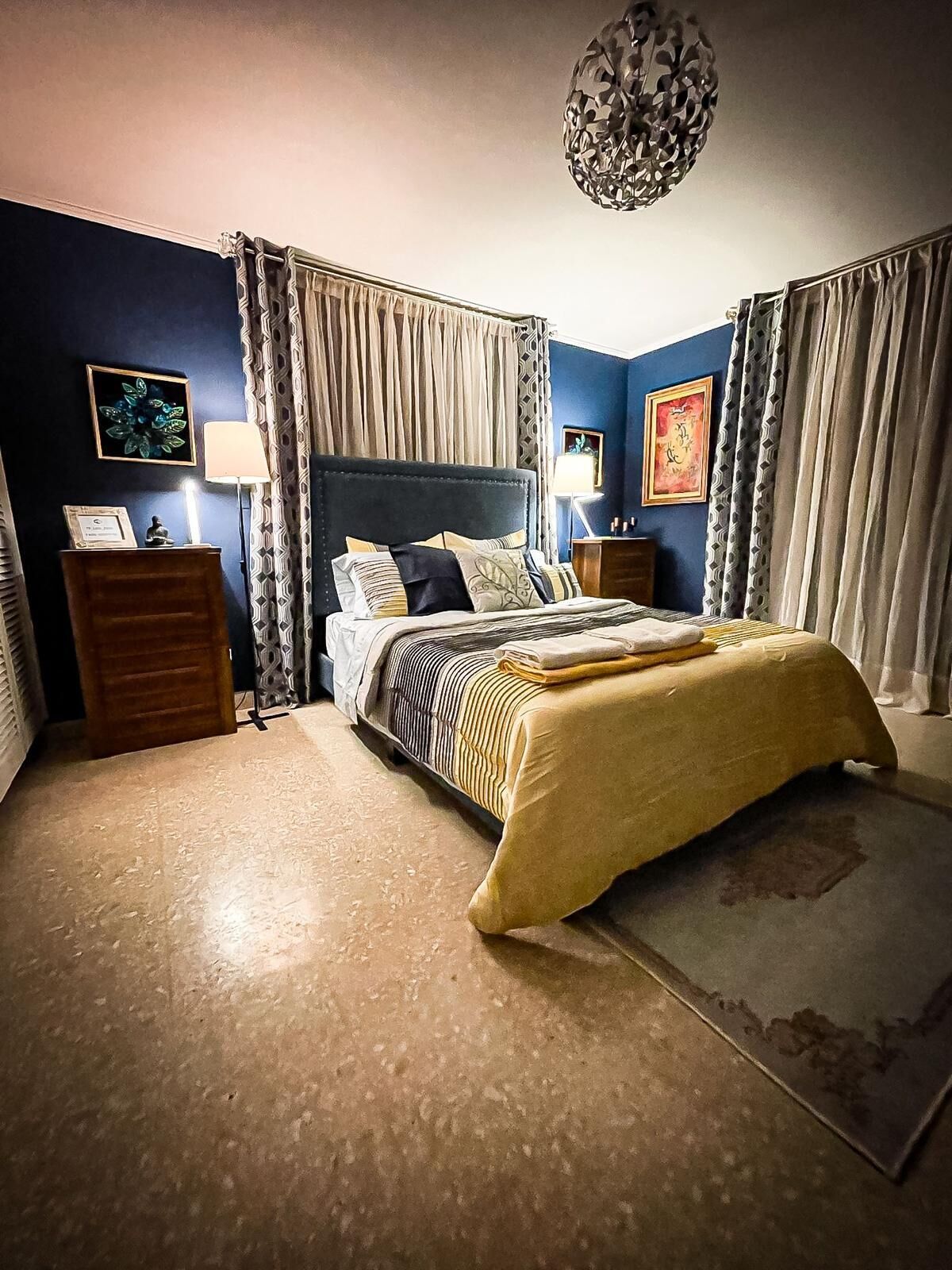 Un dormitorio con cama, mesitas de noche, una lámpara y una luz decorativa en el techo.