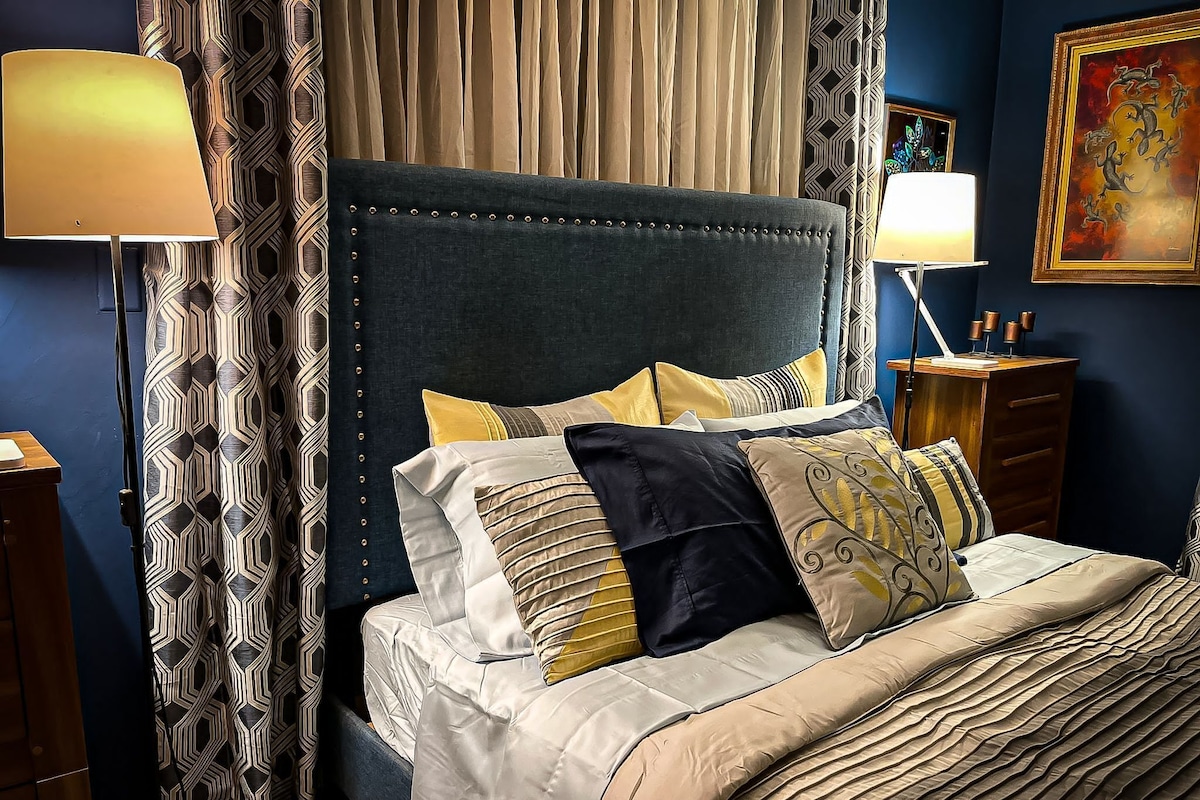 A neatly made bed with a dark headboard, multiple pillows, and a bedside table with a lamp.