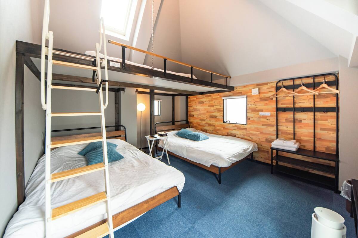 A dormitory room with bunk beds, a loft bed, a wooden wall, and a window.