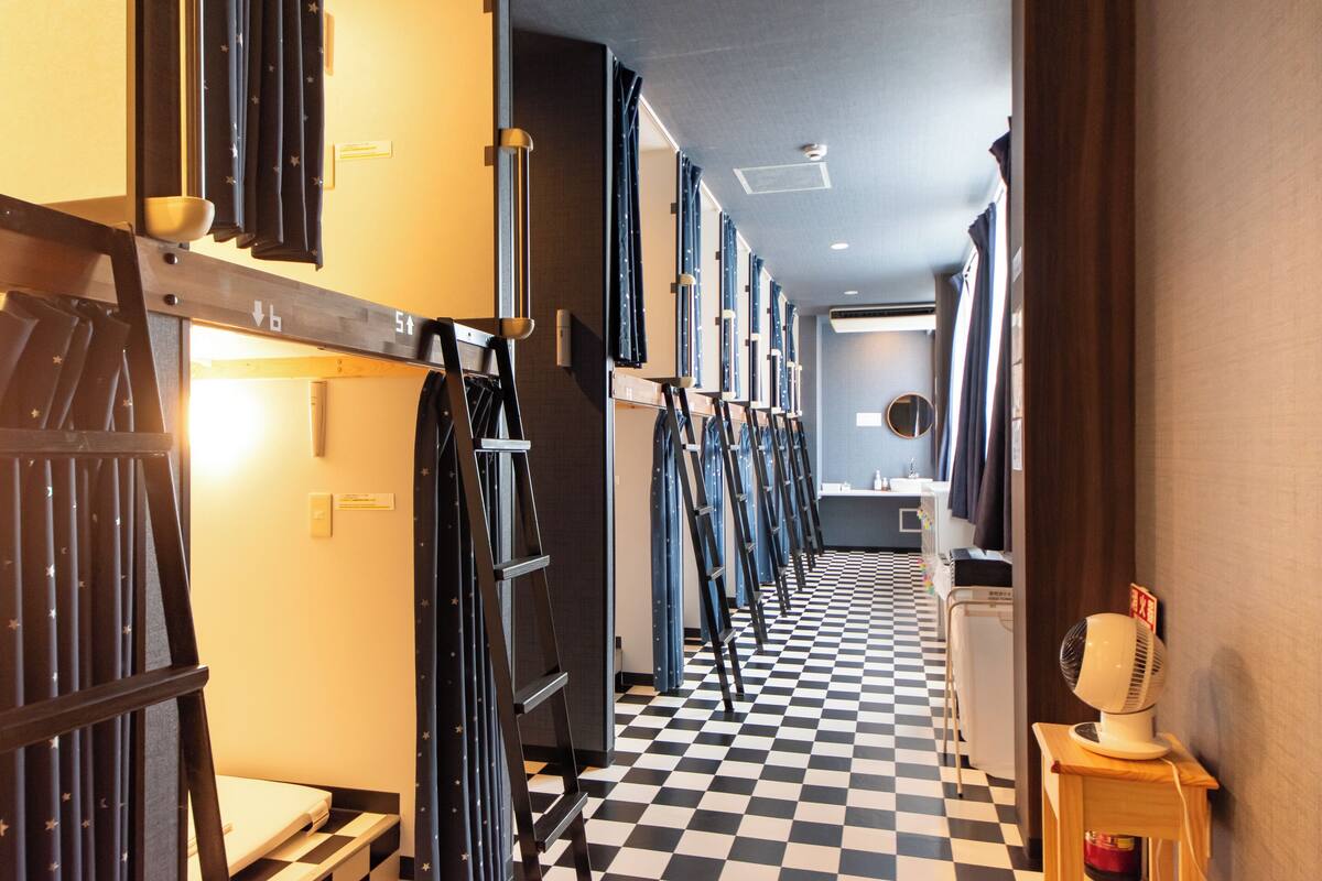 A hotel corridor with checkered flooring, bunk beds, and a fan on a table.