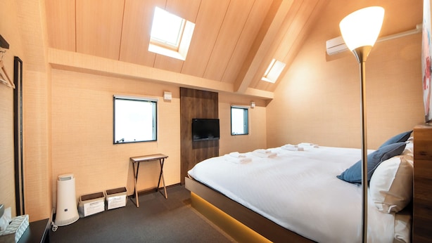 A bedroom with a large bed, a desk, a chair, a TV mounted on the wall, and two windows. - Hotel Base Nara (Nara)