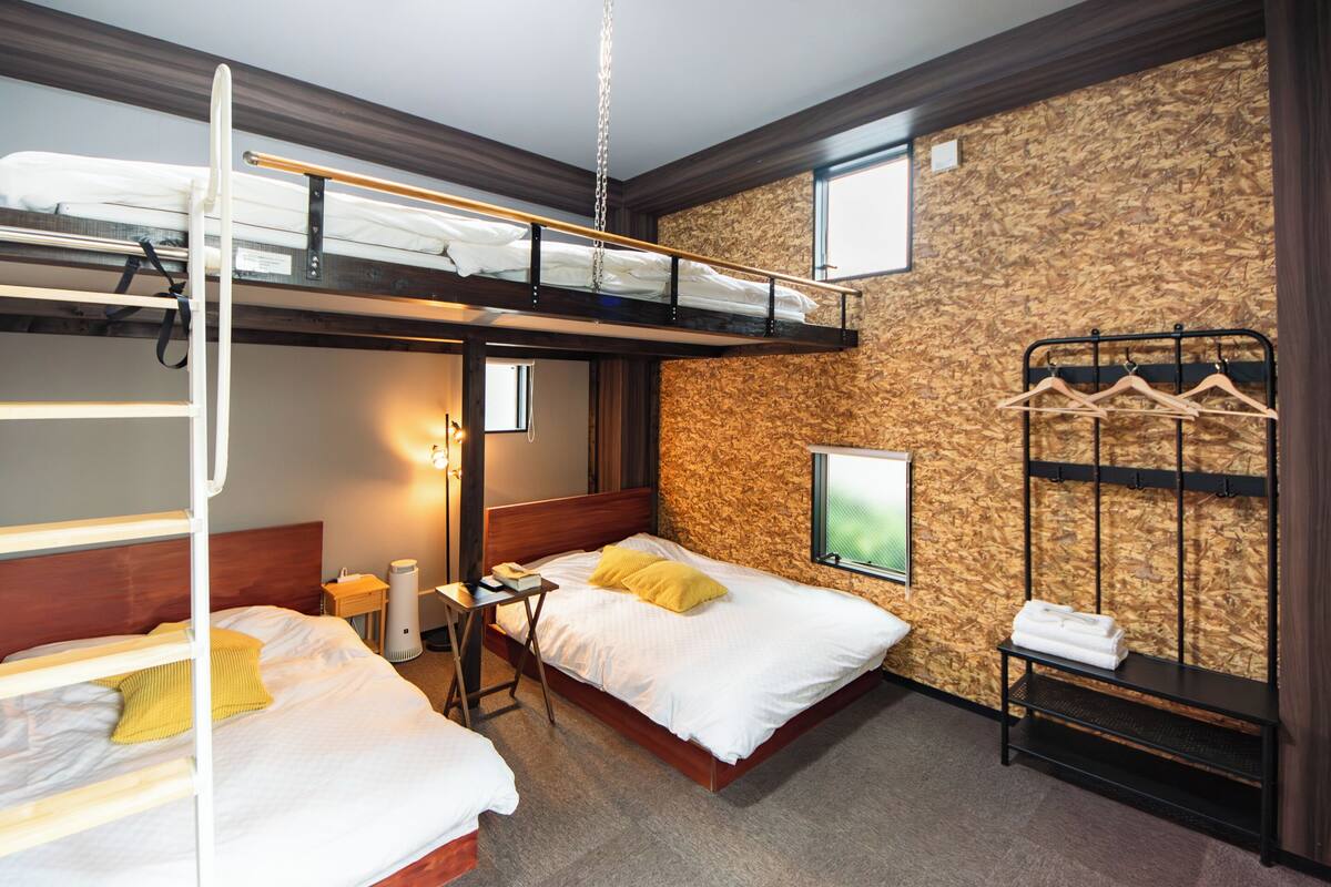 A bunk bed room with a wooden headboard, a desk with a chair, a hanging coat rack, and a small window.