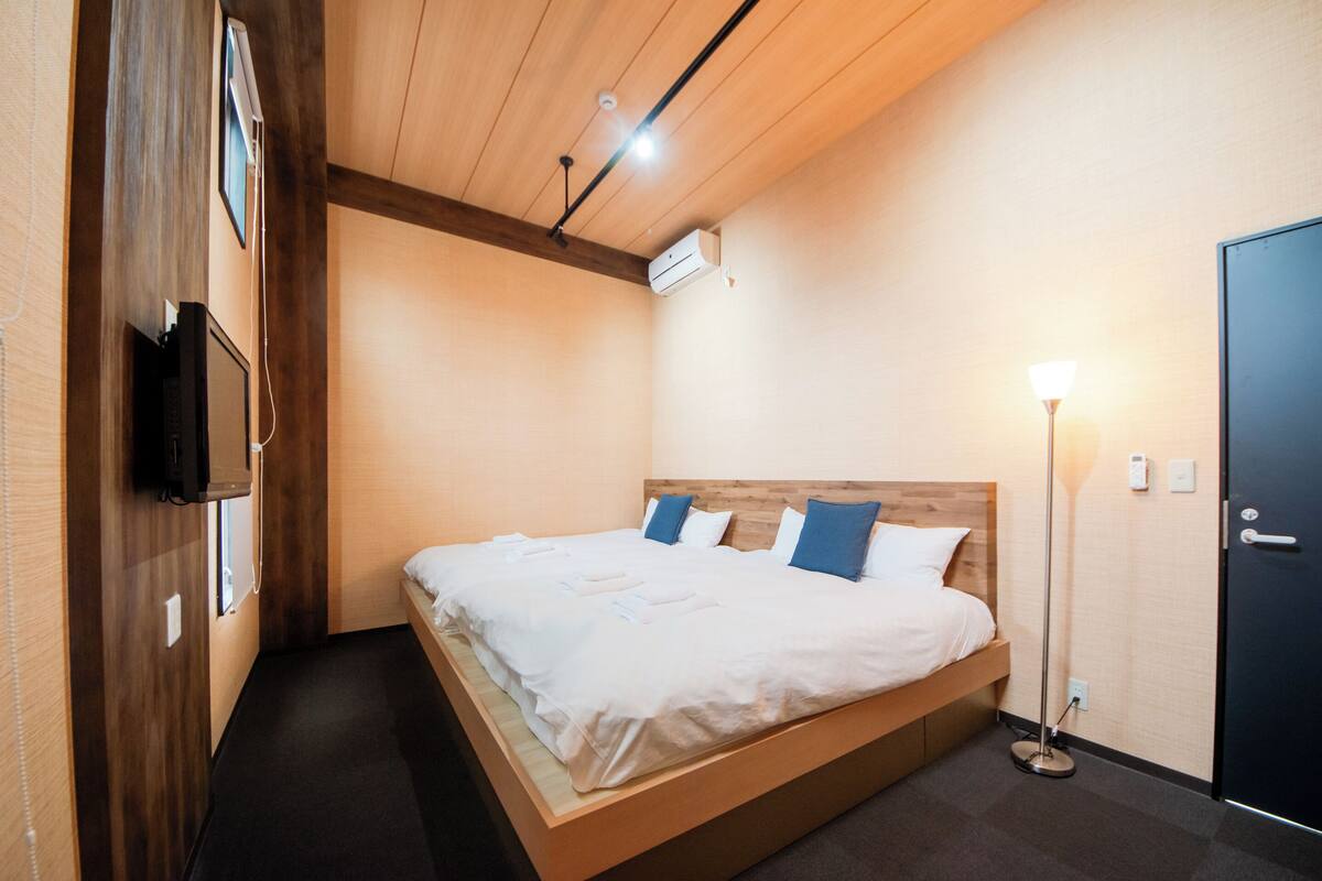 A modern hotel room with a wooden bed, a flat-screen TV, and a bedside lamp.