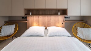 A bedroom with a bed, two chairs, a wooden headboard, and built-in cabinets. - Apartment Happy by Interhome (Cerny Dul/Cista)