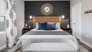 A bedroom with a tufted headboard, patterned bedding, and a decorative mirror above the bed.