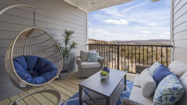 A covered patio with a hanging chair, a cushioned chair, a sofa, and a table with a plant.